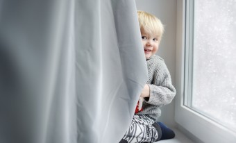 A child playing behind the curtain in their home