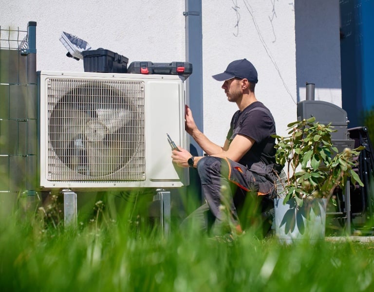 A man installing a heat pump unit outside a house