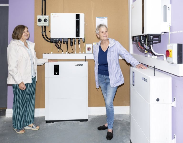 Two women standing with the solar pv battery storage in the Corofin Community Hall.