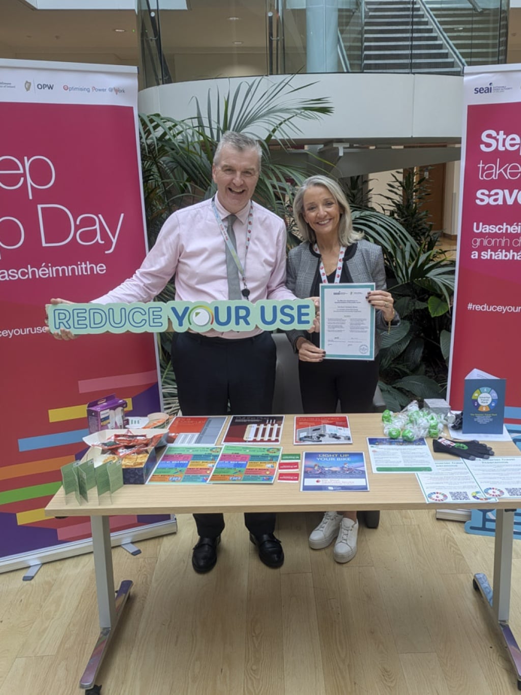 Two people standing at an IBTS stand holding a sign saying 'Reduce Your Use'